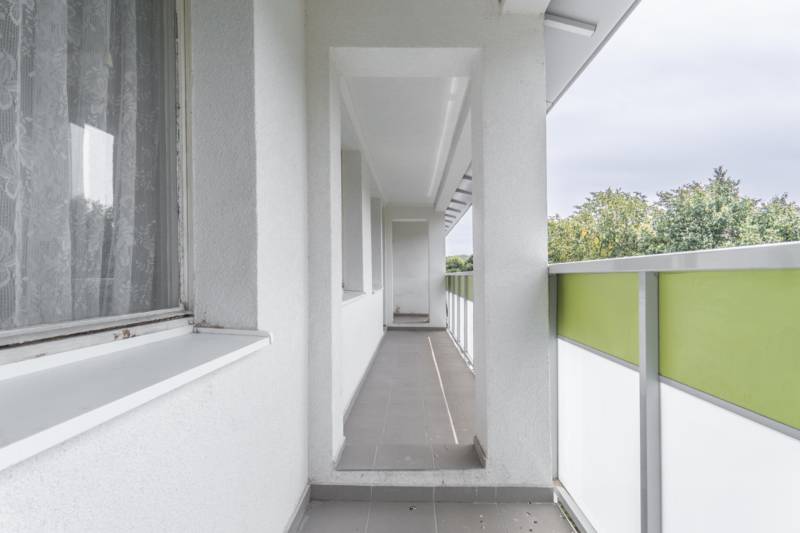Balkón 4-izbového bytu s výhľadom na zeleň, svetlé steny, zelené zábradlie.