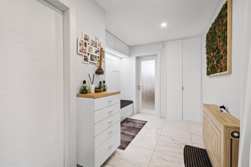 Svetlá predsieň v rodinnom dome s bielym nábytkom a dekoratívnymi prvkami na stenách.