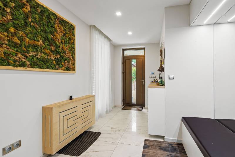 Vstupná hala rodinného domu s panelom machu, veľkými dverami a bielymi stenami.