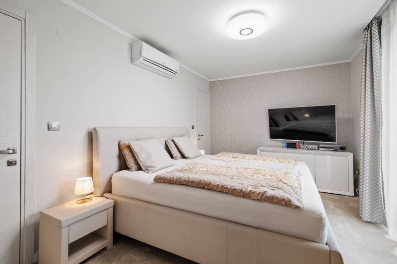 Spálňa s posteľou, televízorom, svetlou stenou a nočným stolíkom v rodinnom dome.