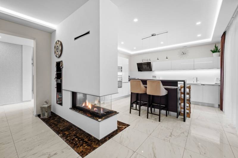 Interiér rodinného domu s krbom, kuchyňou a mramorovou podlahou.