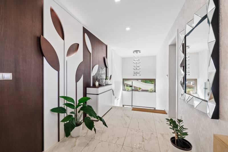 Chodba v rodinnom dome s dekoráciou na stene a rastlinou na keramickej podlahe.