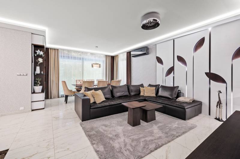 Obývačka s čiernou sedačkou, jedálenským stolom a dekoratívnou stenou v rodinnom dome.