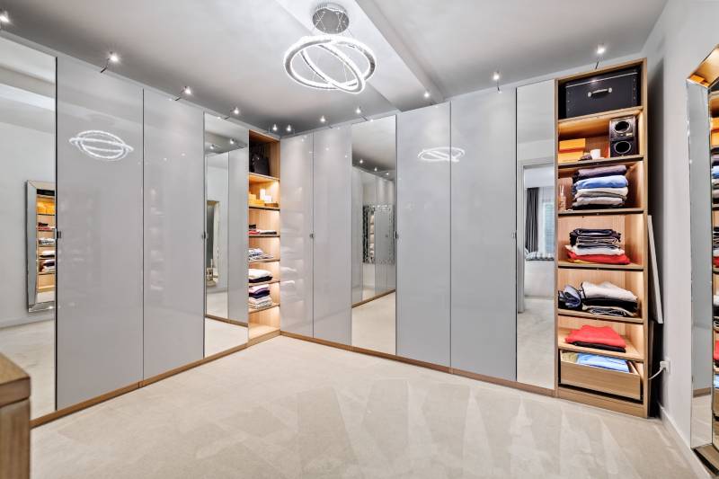 Šatník v rodinnom dome s bielymi skrinkami a dekoratívnym osvetlením.