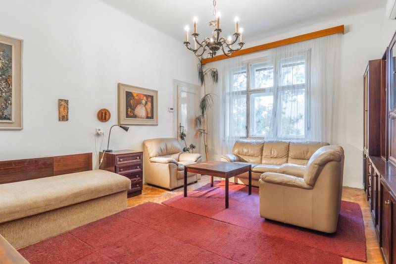 Obývačka v 3-izbovom byte s pohodlnou sedačkou, dreveným dekorom podlahy a červeným kobercom.