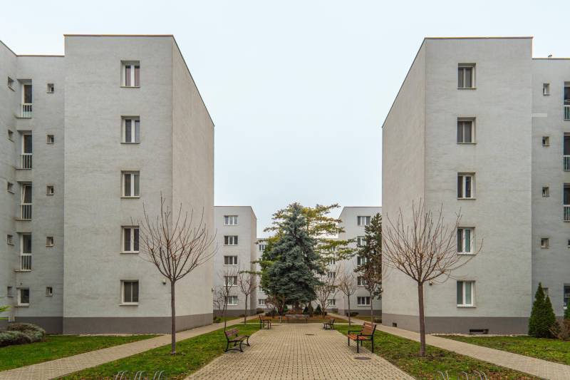 Bytové domy s chodníkom, lavičkami a stromami v lokalite Bratislava - Jurajov dvor, Vajnorská.