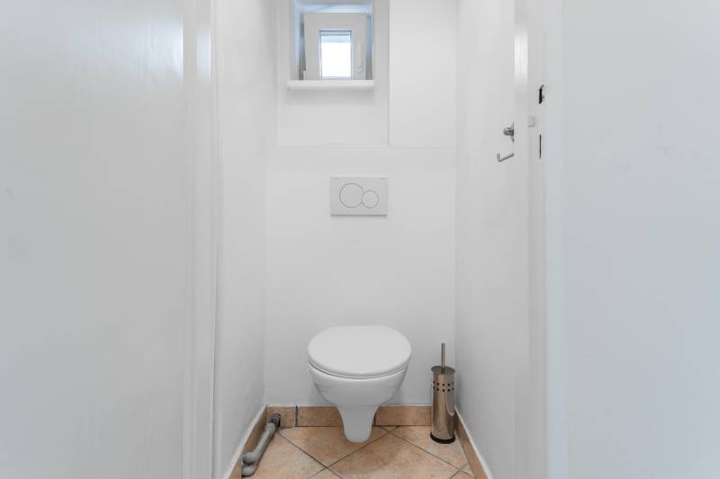 Úzka toaleta v 2-izbovom byte s dlažbou a malým oknom.