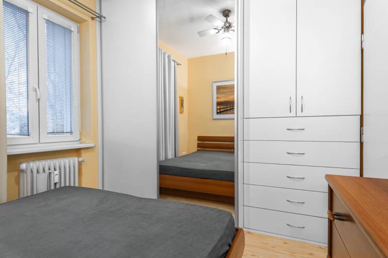 Spálňa s posteľou, bielou skriňou, ventilátorom a dekorom. Podlaha s dreveným dekorom.