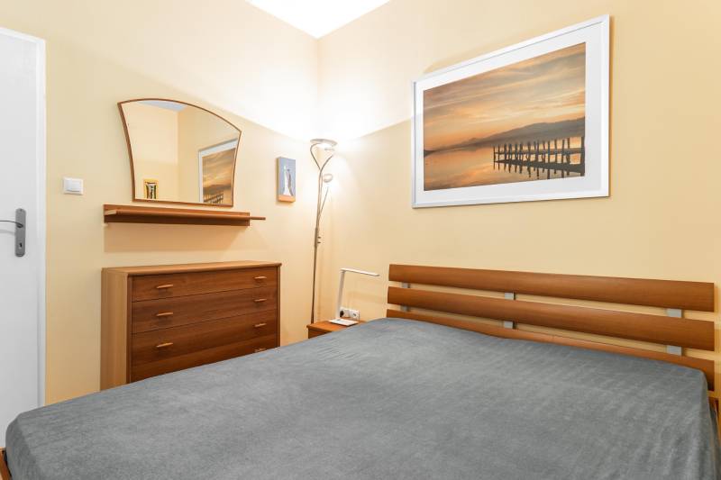 Spálňa v 2-izbovom byte s dreveným nábytkom, zrkadlom a dekoratívnym obrazom.