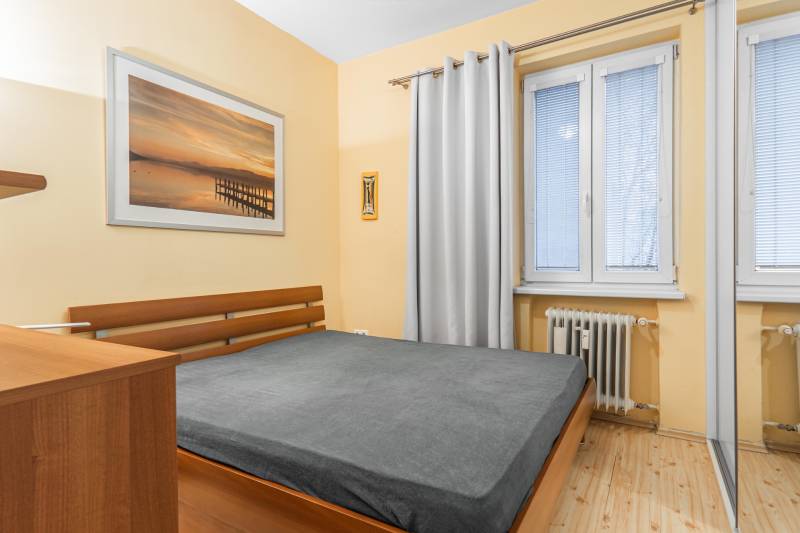 Spálňa s posteľou, podlaha s dreveným dekorom a obrazom v 2-izbovom byte.