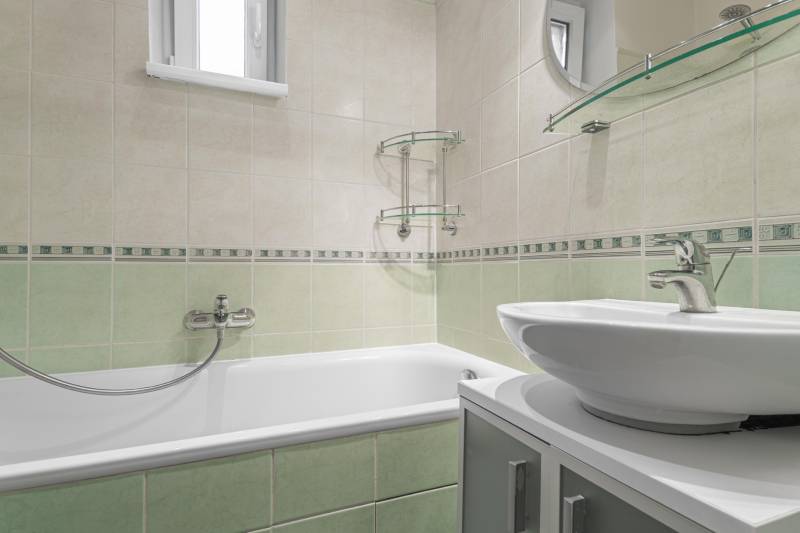 Kúpeľňa v 2-izbovom byte s vaňou, umývadlom a zelenými obkladmi.